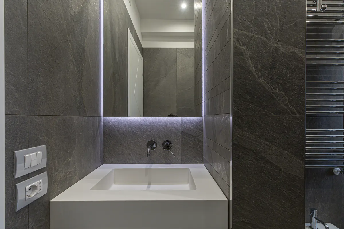 Bagno rivestito in pietra grigia con lavabo a colonna e specchio LED